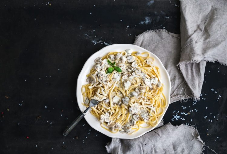 Pasta spaghetti with creamy mushroom sauce and basil in white ceramic plate over old grunge dark table, top view, copy space